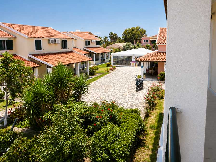 Sun-dappled courtyard of Monika Hotel with weathered blue shutters and terracotta pots of fresh herbs